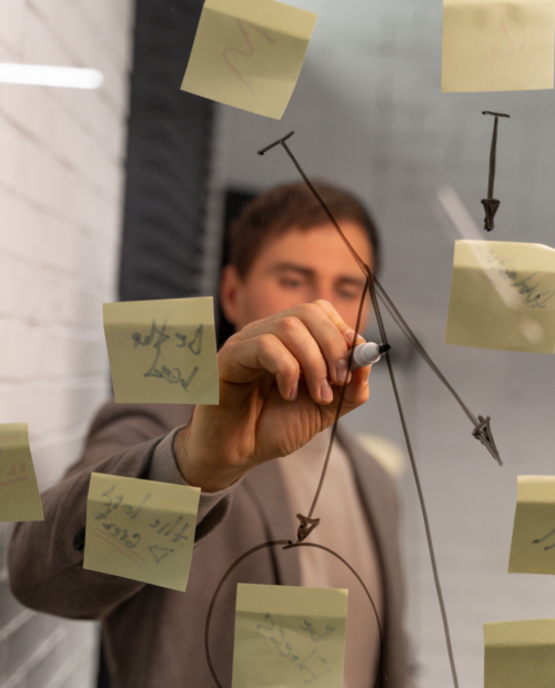 Pessoa escrevendo em um quadro de vidro com post-its colados, focando em planejamento ou brainstorming.