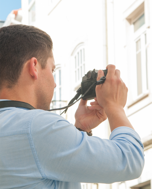 Homem fotografa edifício com máquina fotográfica durante o dia.