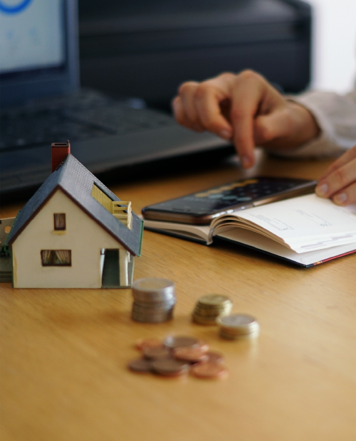 Cálculo da taxa de esforço no crédito habitação com moedas e miniatura de casa.